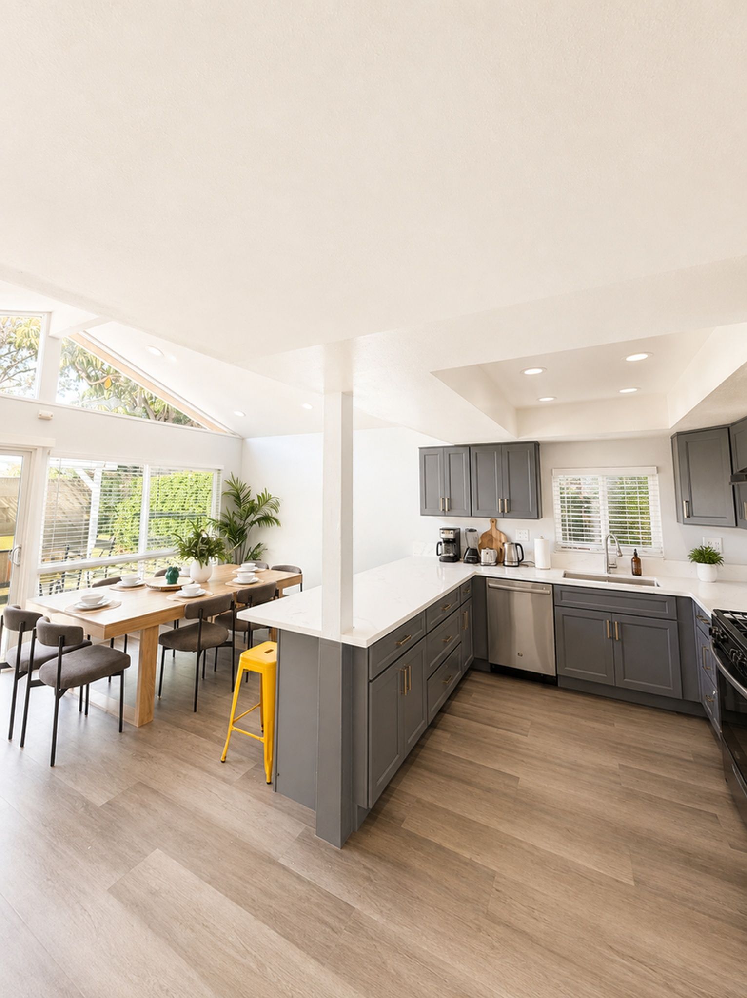 A modern kitchen with grey cabinets, a white countertop, and a wooden dining table with chairs.