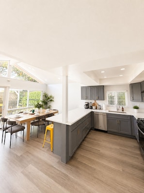 A modern kitchen with grey cabinets, a white countertop, and a wooden dining table with chairs. - Spacious 5-bedroom house in terrific Cypress with BBQ (Cypress)