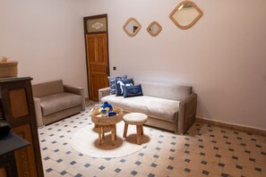 A living room with a sofa, two small stools, a coffee table, and decorative pillows. - Charming 3-bedroom riad in Marrakech with cool AC breeze (Marrakech)