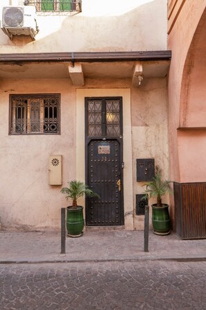 A building with a black door, a window with decorative bars, and two potted plants on the ground. - Charming 3-bedroom riad in Marrakech with cool AC breeze (Marrakech)
