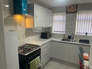 Een kleine keuken met een gasfornuis, een magnetron, een spoelbak en een raam met zonwering.