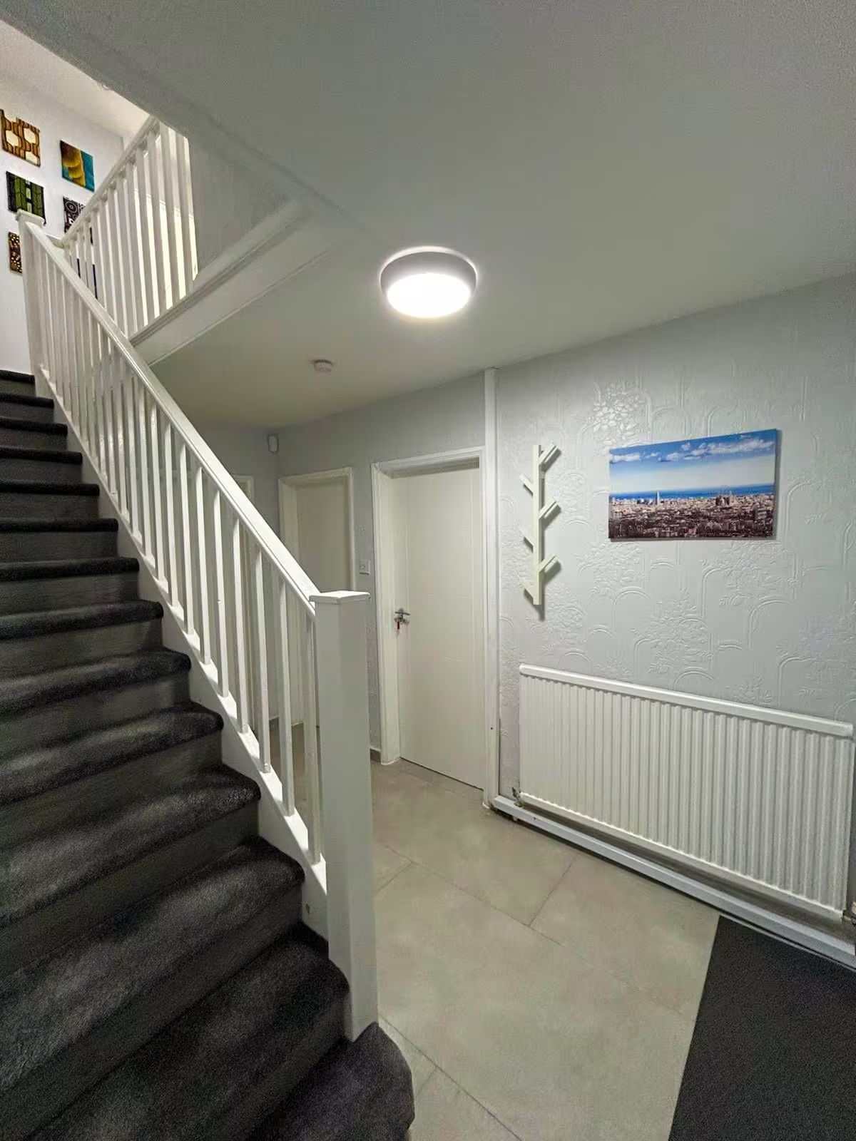 A staircase with white railings leading to a landing, a radiator on the wall, and a framed picture of a cityscape.