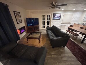 A living room with a sofa, a coffee table, a television, and a fireplace. - Spacious 2-bedroom back-house of duplex with sunroom in charming Talent (Talent)