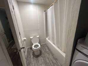 Une salle de bain équipée de toilettes, d’un rideau de douche et d’un lave-linge Samsung.
