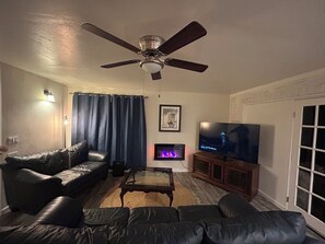 Un salon doté d’un ventilateur de plafond, d’un canapé en cuir, d’une télévision et d’une cheminée.