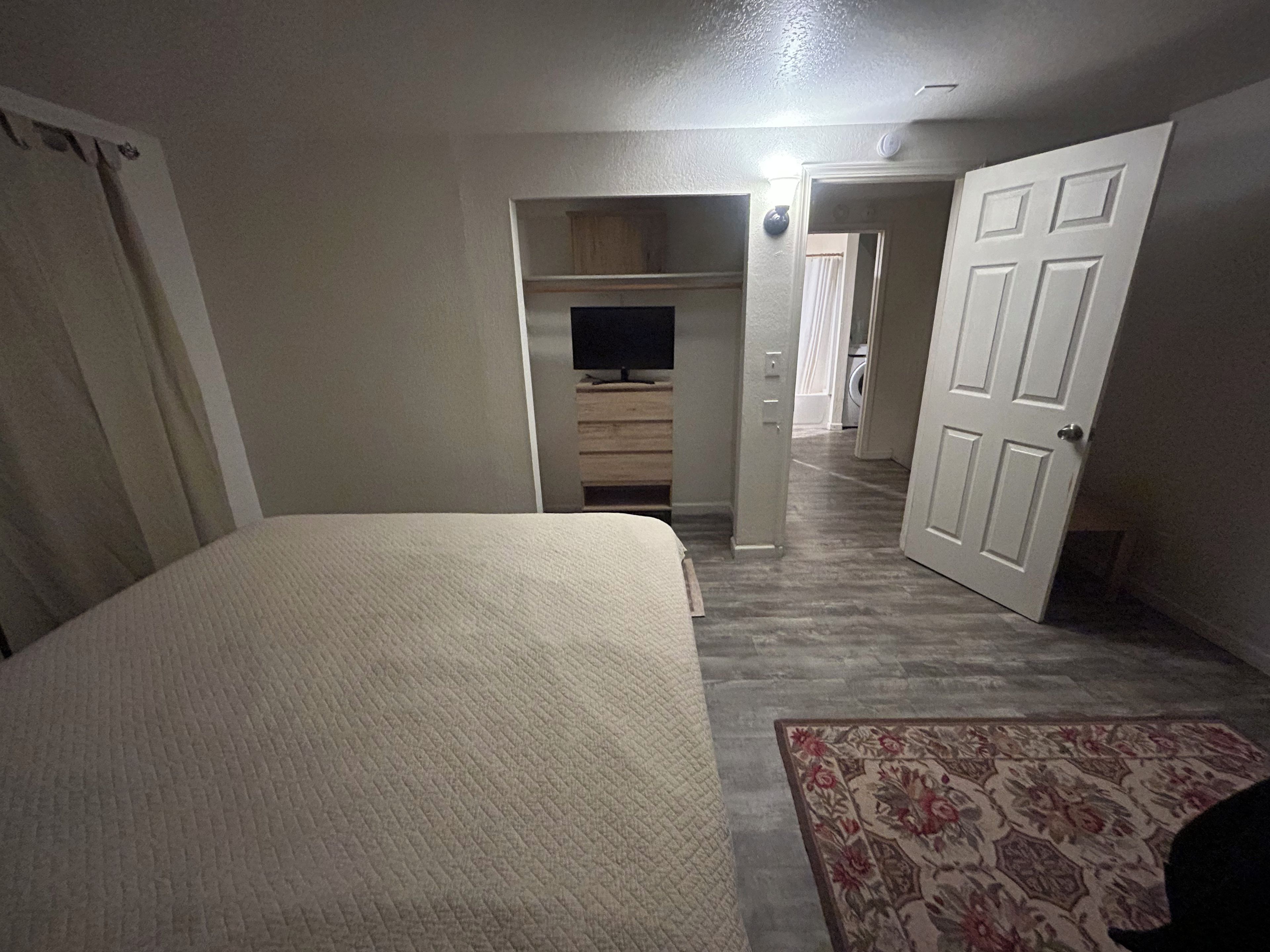 A bedroom with a bed, a television, a wardrobe, and a door leading to another room.