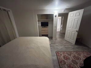 Une chambre à coucher comprenant un lit, une télévision, une armoire et une porte donnant sur une autre pièce.