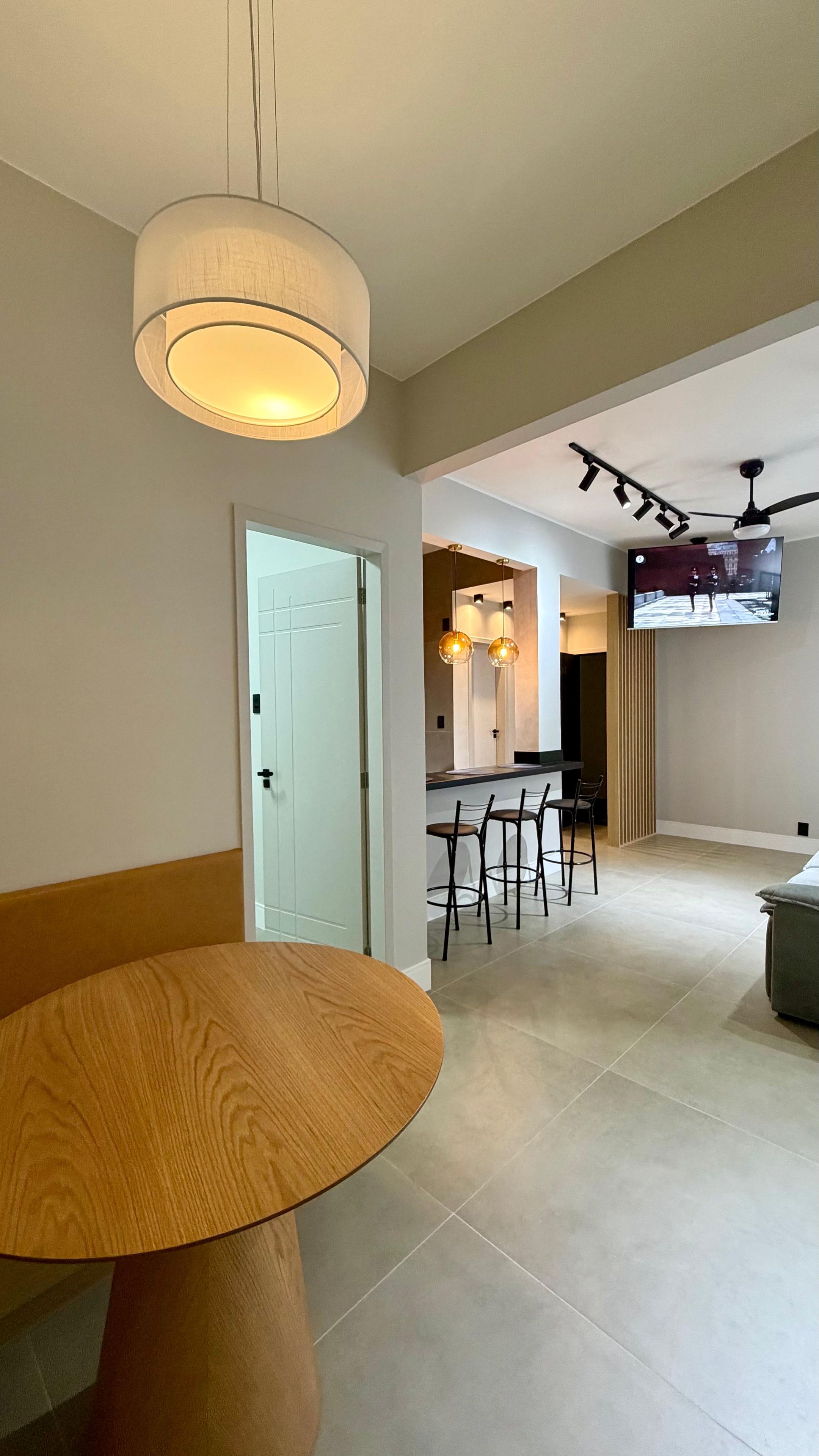A modern kitchen with a dining area, a ceiling fan, and a TV mounted on the wall.