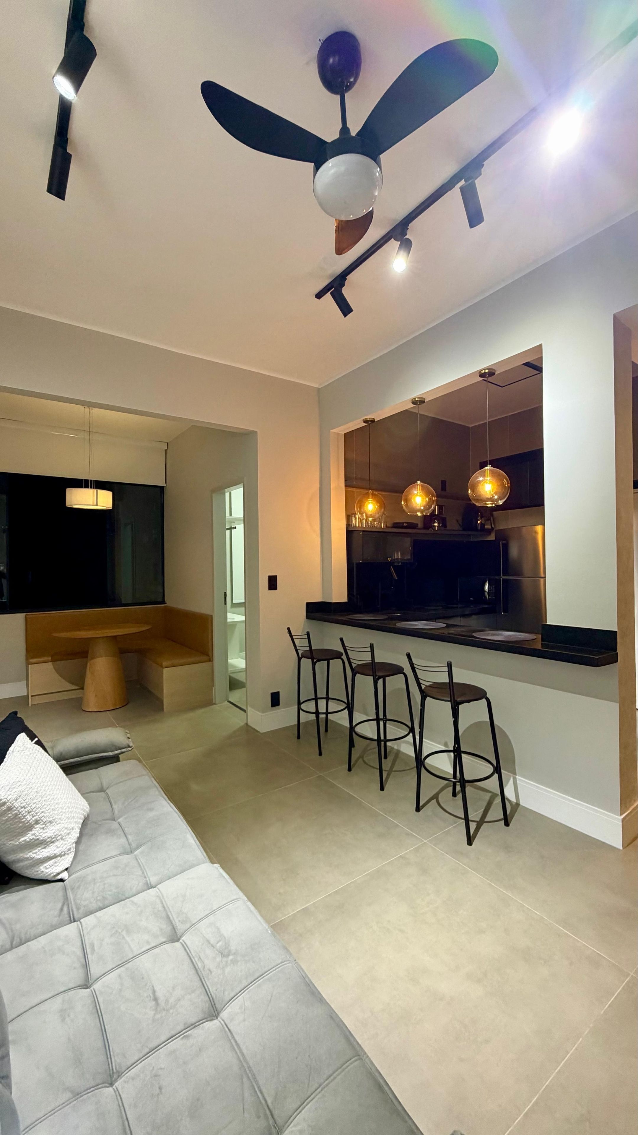 A modern kitchen with bar stools, a dining area with a sofa, and a ceiling fan.