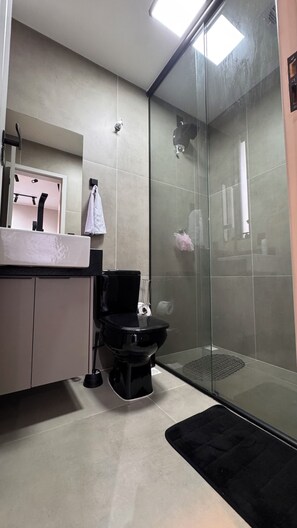 A modern bathroom with a glass shower enclosure, a toilet, a sink, and a mirror. - Lapa RJ Space | Style and Comfort in Lapa (Rio de Janeiro)