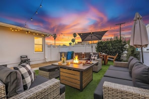 An outdoor patio with a fire feature, seating, and string lights against a sunset sky. - Pacific Beach Bungalow - Walk to Dine, Shop and Surf (San Diego)