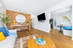 A modern living room with a sofa, coffee table, and a TV mounted on the wall. - Pacific Beach Bungalow - Walk to Dine, Shop and Surf (San Diego)