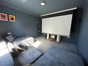 A cozy room with a large white screen, a fireplace, and comfortable seating. - Sheringham Luxury, Cinema, Hot Tub & Beach (Norfolk)