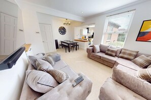A modern living room with sofas, a dining area, and a kitchen in the background. - Sheringham Luxury, Cinema, Hot Tub & Beach (Norfolk)
