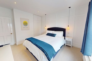 A hotel room with a bed, a nightstand, a lamp, a door, and a wall with a framed picture. - Sheringham Luxury, Cinema, Hot Tub & Beach (Norfolk)