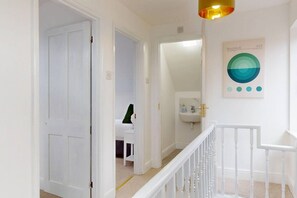 A hallway with white walls, a white door, a staircase with white railings, and a wall-mounted light fixture. - Sheringham Luxury, Cinema, Hot Tub & Beach (Norfolk)