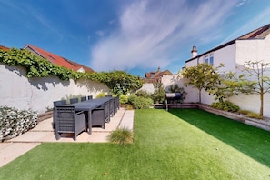 A backyard with a dining table and chairs, a barbecue grill, and a well-maintained lawn. - Sheringham Luxury, Cinema, Hot Tub & Beach (Norfolk)
