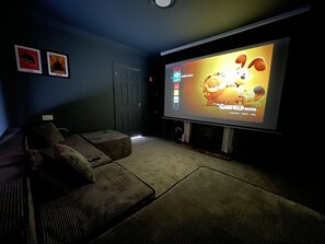 Una sala home theater con un grande schermo piatto, un divano reclinabile e un pavimento tappezzato.
