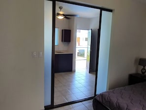 A room with a sliding door leading to a balcony, a ceiling fan, a bed, and a nightstand with a lamp. - Marina Loft Condo #212 (Sardinal)