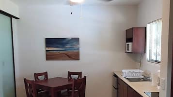 A compact kitchen with a dining table, chairs, a ceiling fan, a microwave, and a window with blinds.