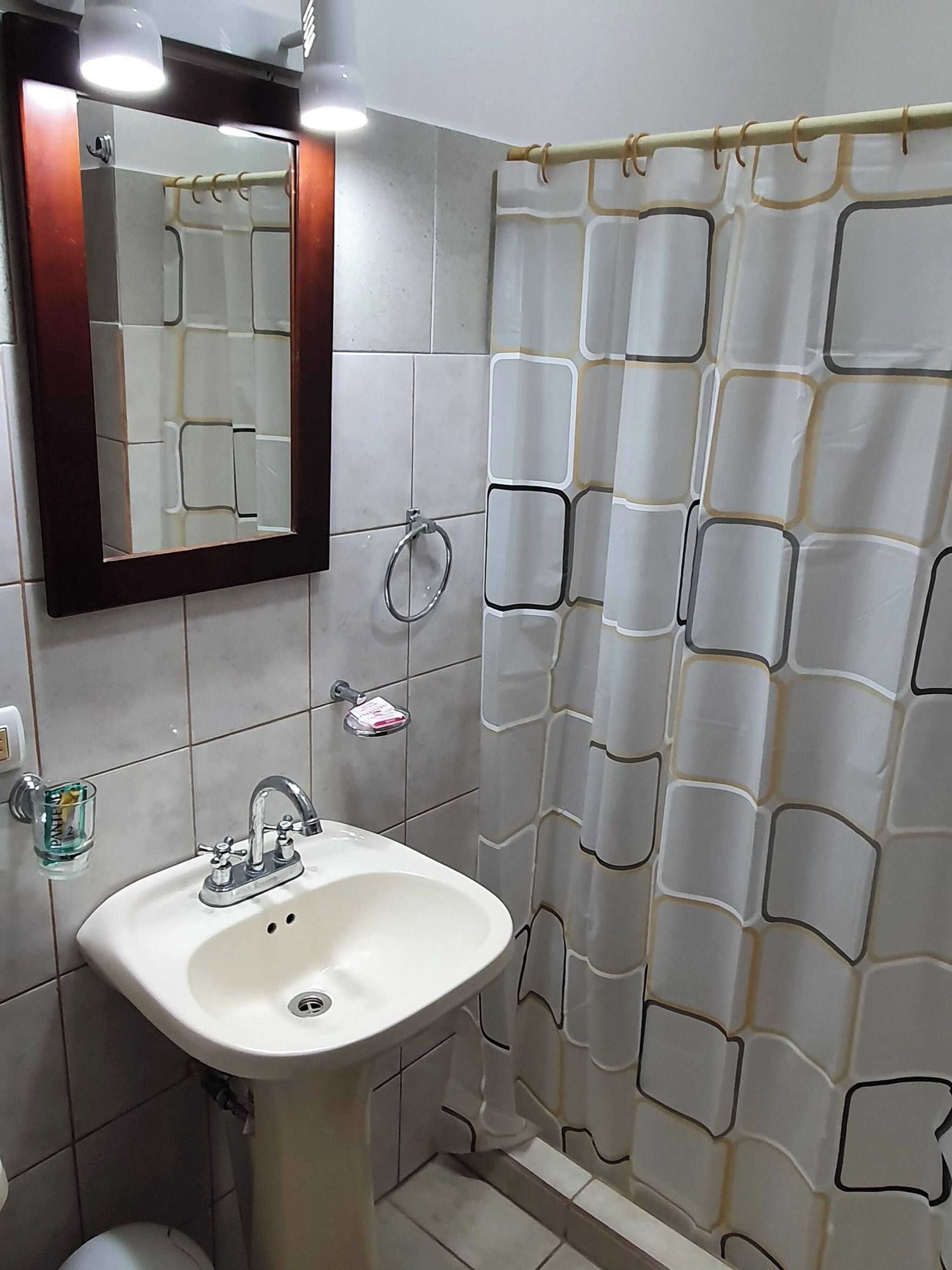 Un baño con un lavamanos blanco, un espejo, una cortina de ducha y un inodoro.