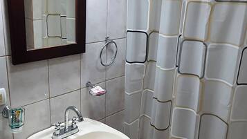 Un baño con un lavamanos blanco, un espejo, una cortina de ducha y un inodoro.