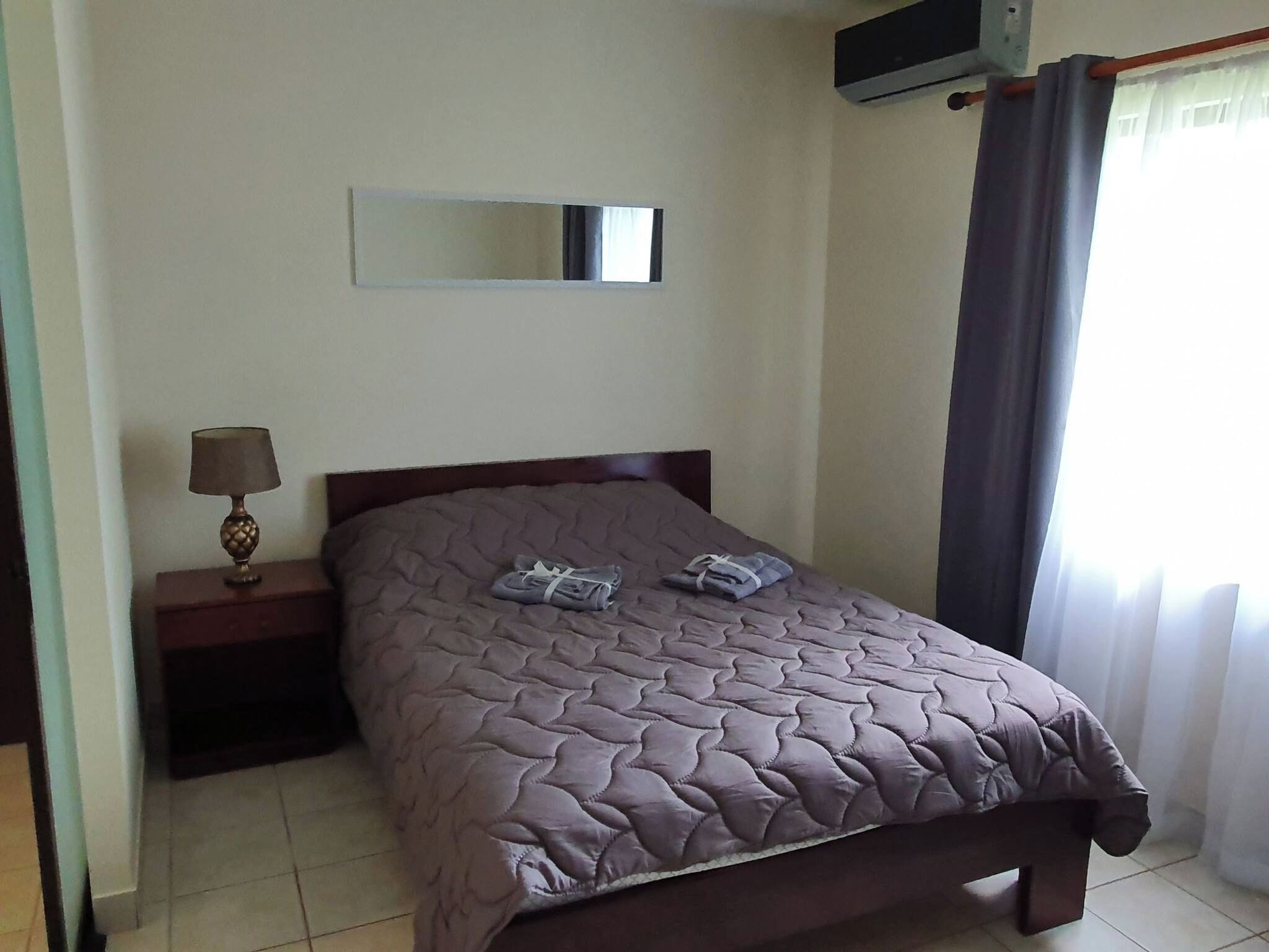 Una camera da letto con un letto, un comodino, una lampada, uno specchio e una finestra con tende.
