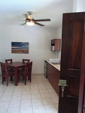 Un comedor con una mesa, sillas, un ventilador de techo, un microondas y una puerta.