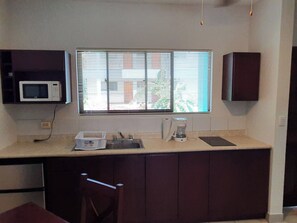 A kitchen with a microwave, a sink, a coffee maker, and a window with blinds. - Marina Loft Condo #212 (Sardinal)