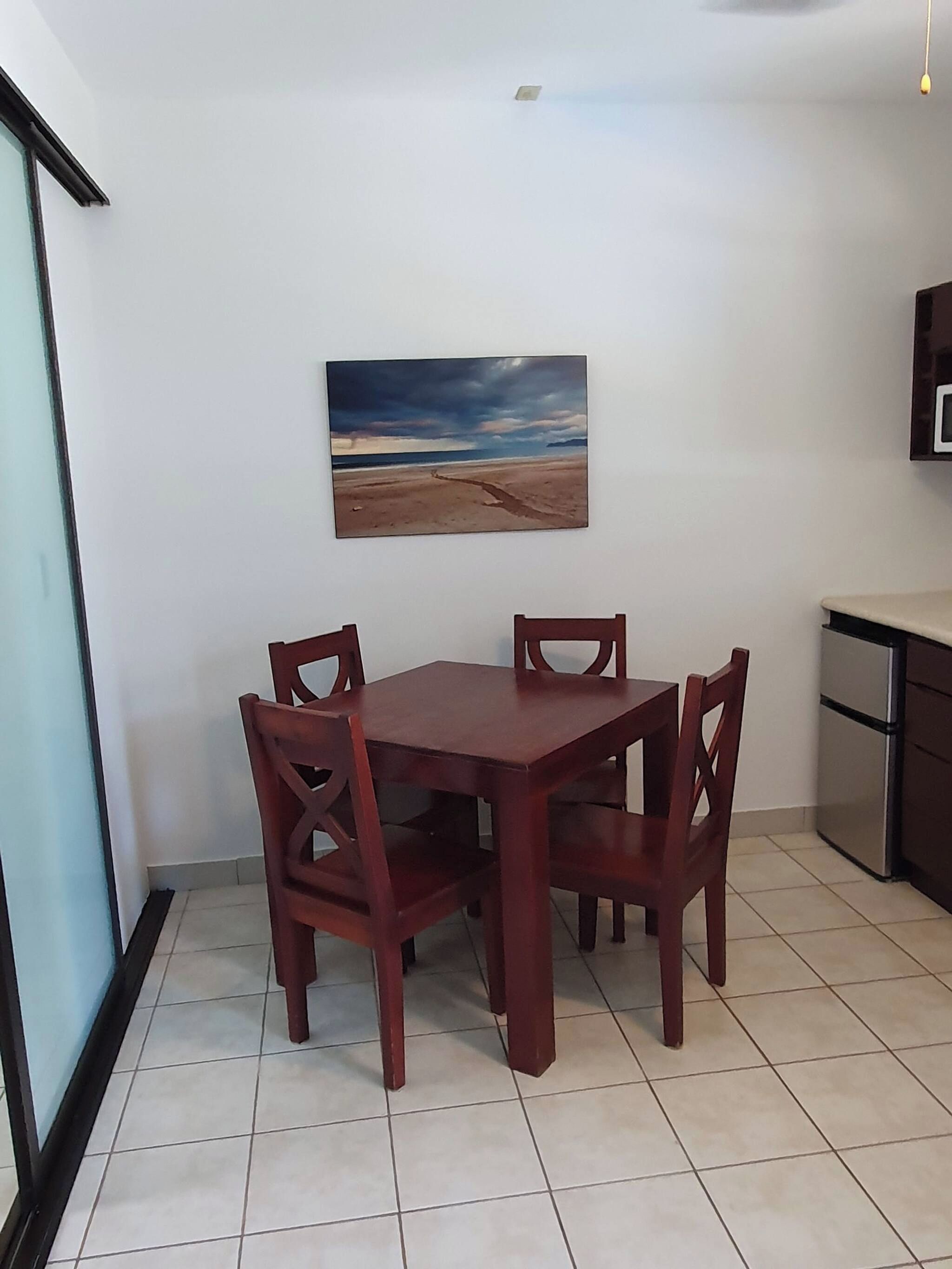 Zona pranzo con tavolo e sedie, un quadro appeso al muro e angolo cottura.