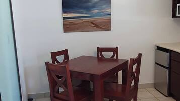 Zona pranzo con tavolo e sedie, un quadro appeso al muro e angolo cottura.