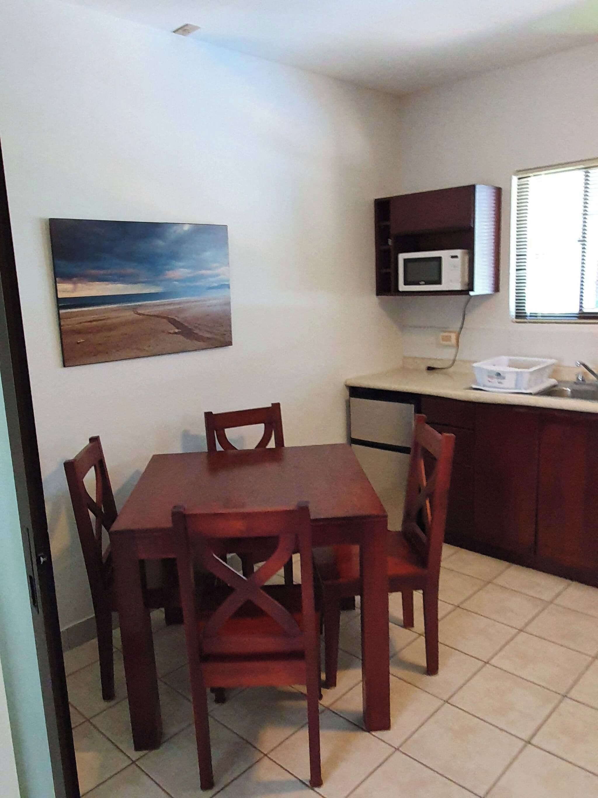 Espaço de refeições com mesa e cadeiras, um quadro na parede, micro-ondas e janela com persianas.