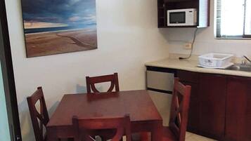 Espaço de refeições com mesa e cadeiras, um quadro na parede, micro-ondas e janela com persianas.