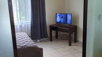 Una habitación con una cama, un televisor sobre un mueble bajo y una ventana con cortinas.