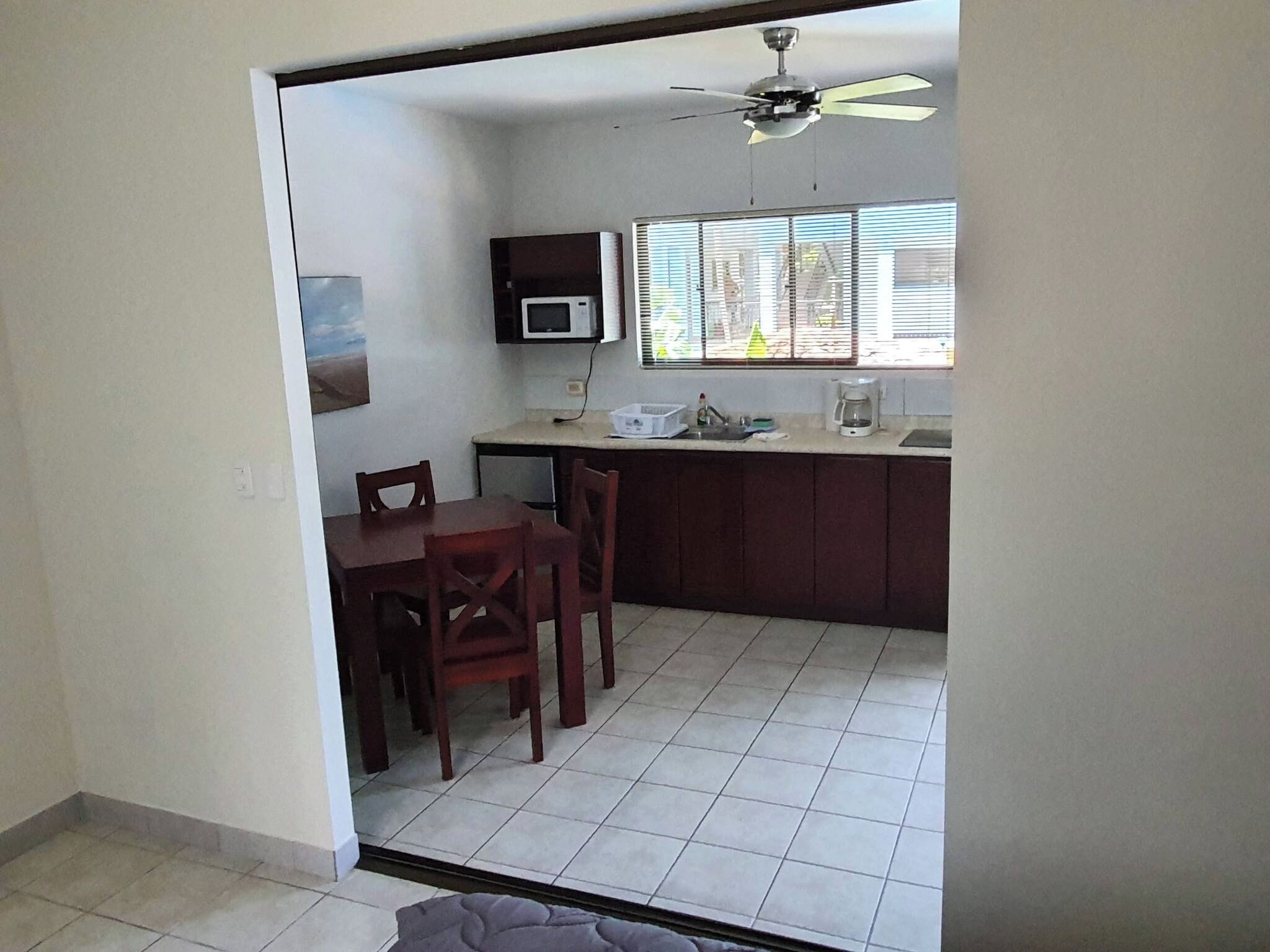 A compact kitchen with a dining area, a ceiling fan, and a window with blinds.
