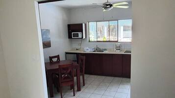 A compact kitchen with a dining area, a ceiling fan, and a window with blinds.