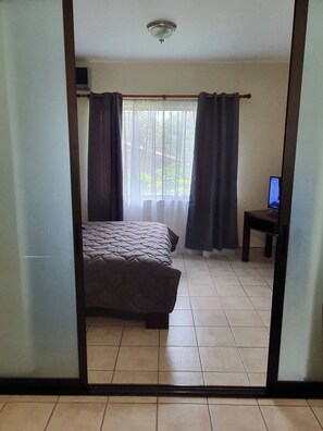 Un dormitorio con cama, cortinas, una mesita y un televisor.
