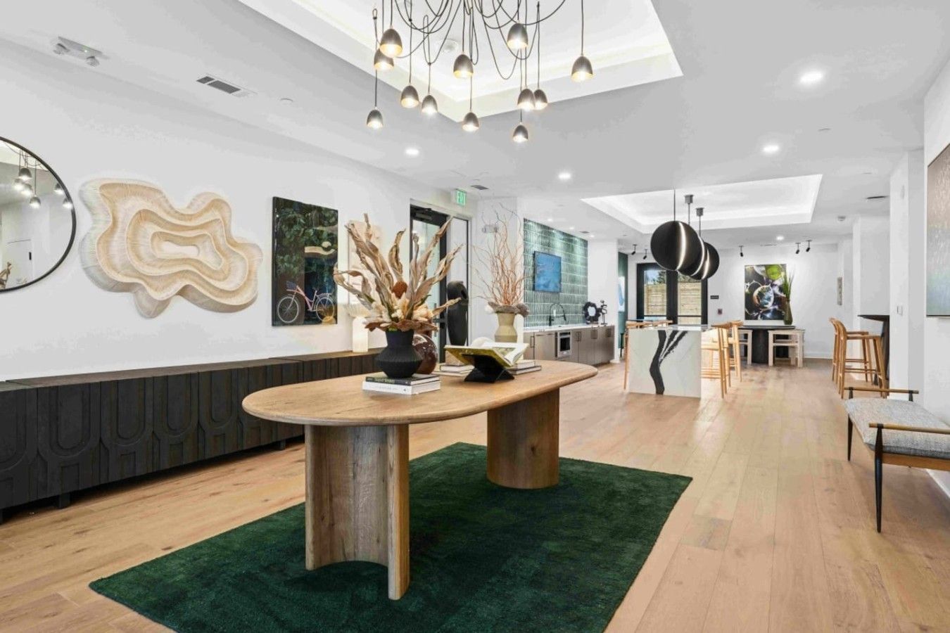 Een modern interieur met een ronde houten tafel, een groen vloerkleed en een keuken op de achtergrond.