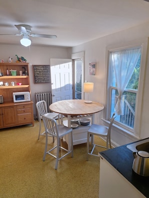 A room with a round table, chairs, a microwave, a radiator, a ceiling fan, and a window with curtains. - Peaceful 2-bedroom house in  Evanston. (Evanston)
