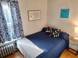 A bedroom with a bed, a radiator, a window with curtains, a wall-mounted picture, and a bedside table with a lamp. - Peaceful 2-bedroom house in  Evanston. (Evanston)