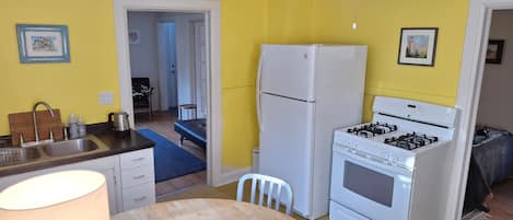 A compact kitchen with a refrigerator, stove, and sink. There is a dining table with chairs.