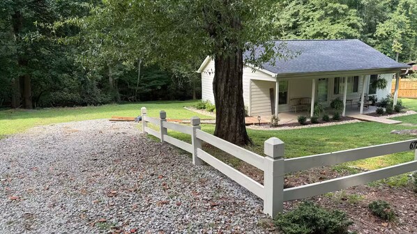 A house with a porch, a gravel driveway, and a white fence.