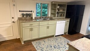 A kitchen with light green cabinets, a double sink, a dishwasher, and a black refrigerator.