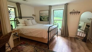 Un dormitorio con una cama individual, una silla, una mesita de noche, un espejo y una ventana con cortinas.