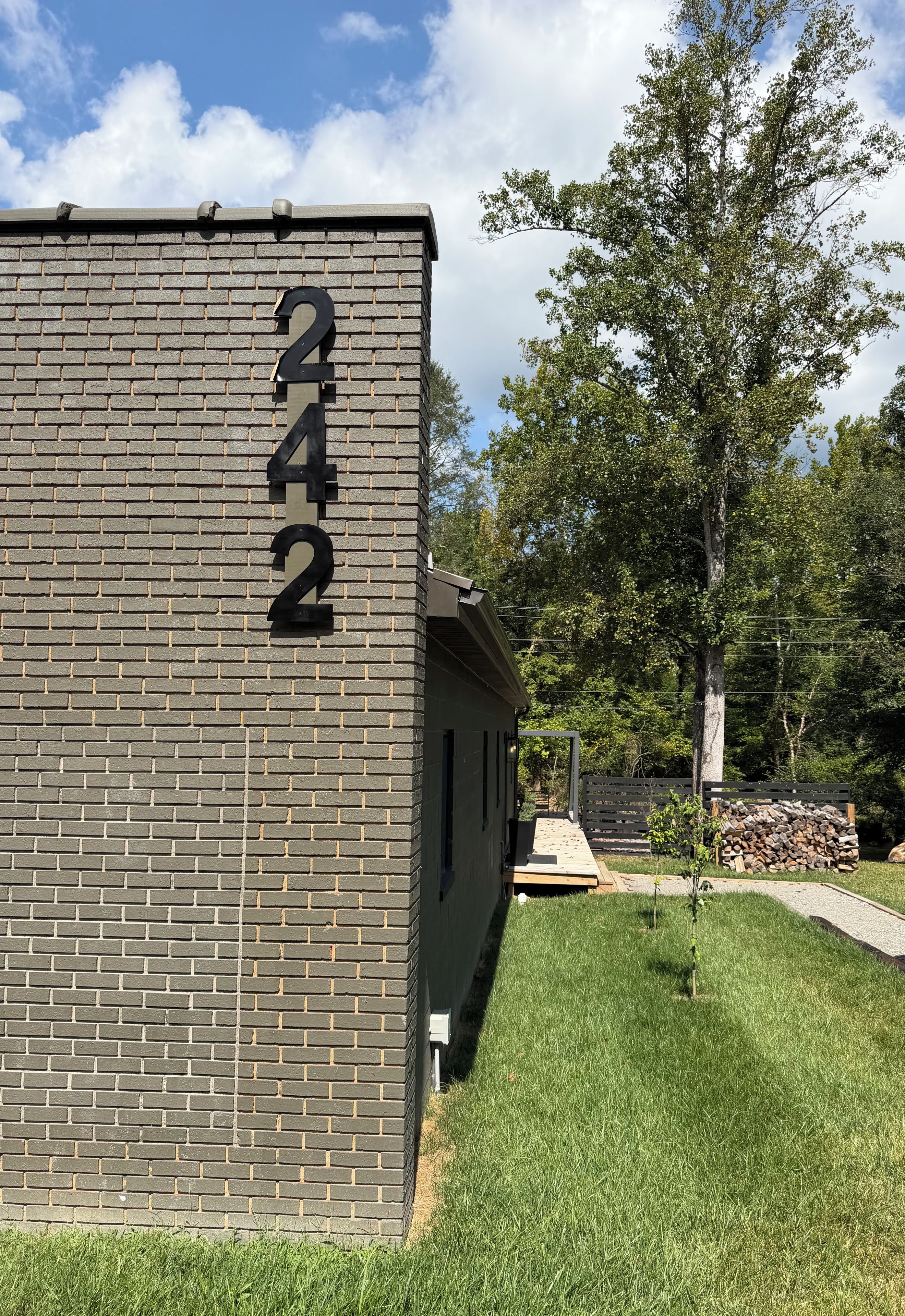A brick building with the number 242 on its side, a grassy yard, and trees in the background.