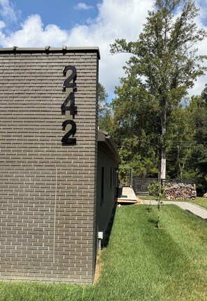 Un edificio de ladrillo con el número 242 en la fachada, un patio cubierto de césped y árboles al fondo.