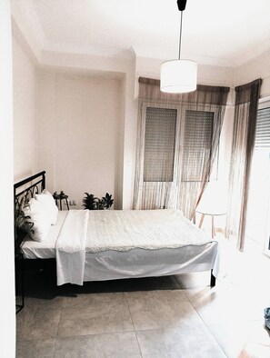 A bedroom with a bed, a bedside table, a hanging light fixture, and a window with curtains. - Candy Studio Marousi (Marousi)