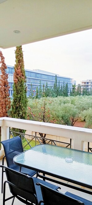Ein Sitzbereich im Freien mit Tisch und Stühlen, mit Blick auf einen angelegten Garten und moderne Gebäude.