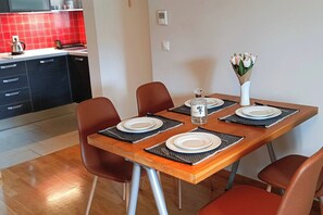 Mesa de comedor dispuesta con platos, cubiertos y una botella, rodeada de sillas.