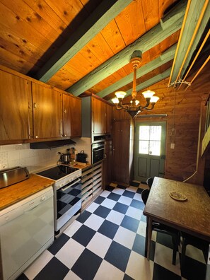 A kitchen with wooden cabinets, a black and white checkered floor, a chandelier, and a window with curtains. - Comfortable chalet for nature lovers - near Portes du Soleil skiing area (Val-d'Illiez)